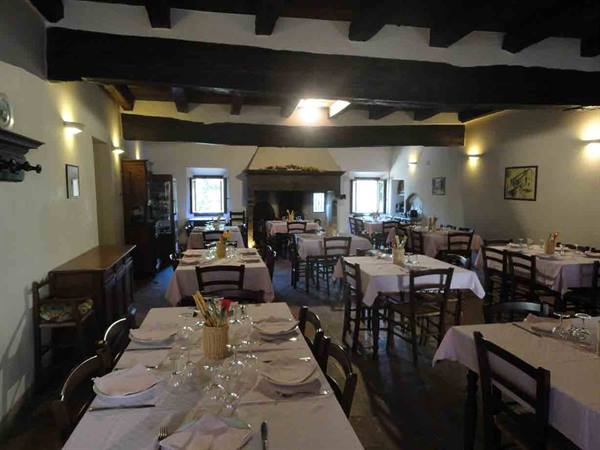 Trattoria dining room with white-clothed tables, wooden beams and fireplace