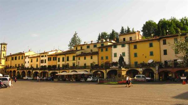 People strolling past colorful arcaded buildings and a statue in Greve in Chianti square