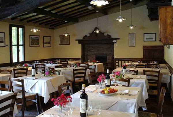 Trattoria dining room with set tables, wine bottles, flowers and brick fireplace