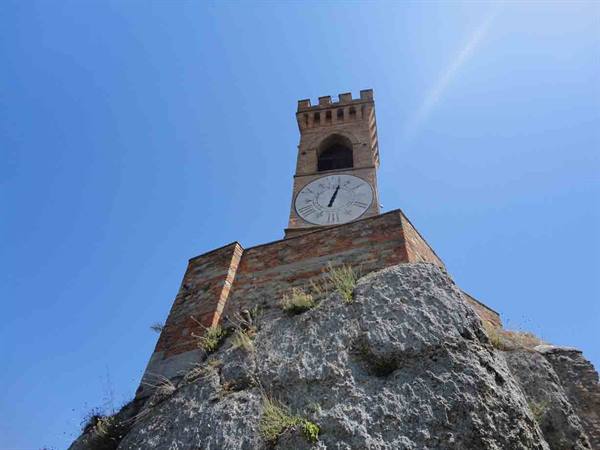 Brick clock tower rising from a rock against blue sky, Brisighella