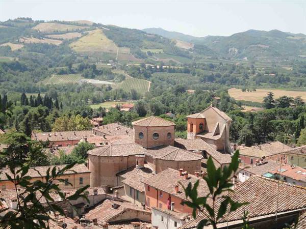 Brick rooftops and round church among cultivated hills in midday light