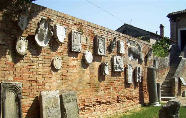 Stone coats of arms and plaques set in a brick wall, staircase nearby