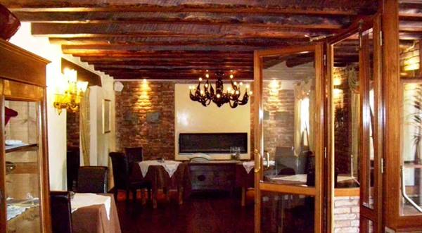 Restaurant dining room with wooden beams, black chandelier, set tables and brick walls