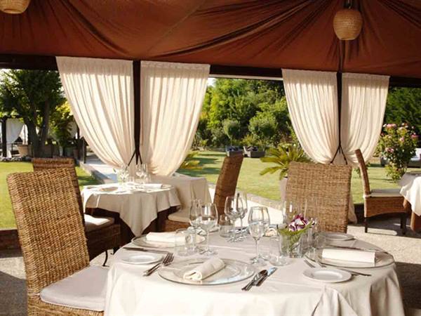 Set table with glasses and wicker chairs under canopy with white drapes