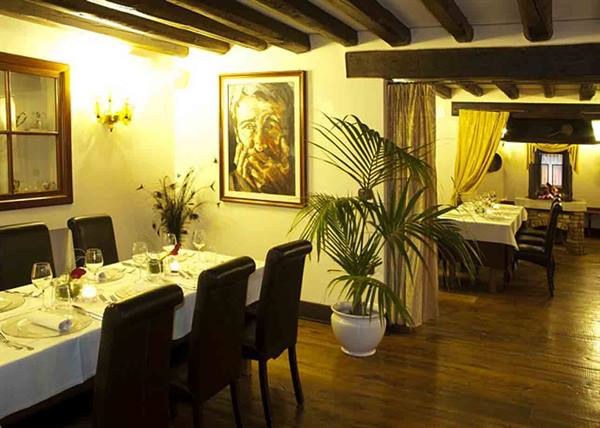 Restaurant dining room with wooden beams, set tables, potted palm and painting