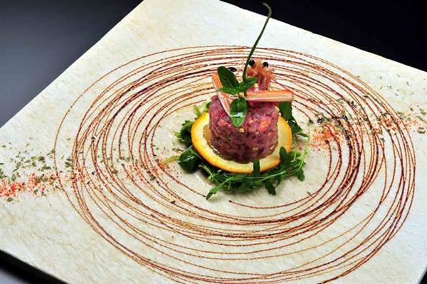 Tuna tartare on stone plate, decorated with sauce spirals and mint