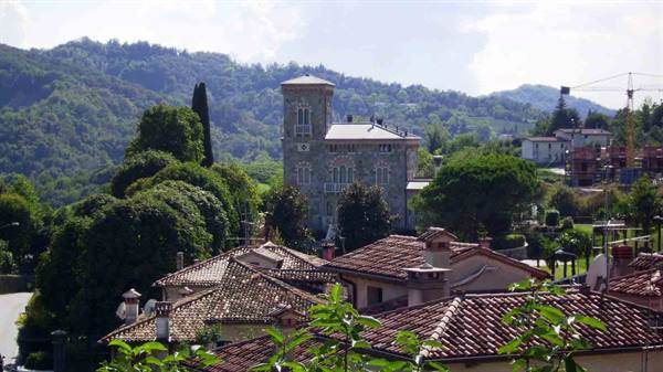 Stone villa with tower above terracotta rooftops amid green hills