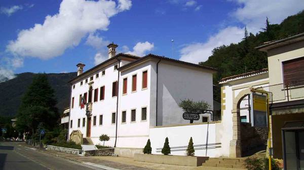 White seminary building with arched entrance, green mountains and cloudy sky