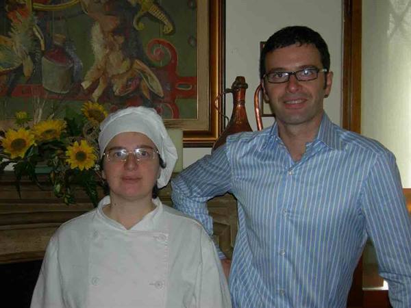 Cook in white uniform beside a man in a striped shirt, fireplace with sunflowers
