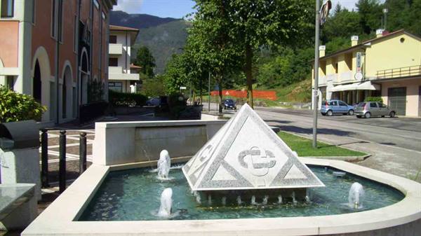 circular fountain with marble pyramid, water jets, town square with cars