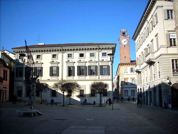 Piazza Cavour in Vercelli, yellow palace and clock tower, people walking, blue sky