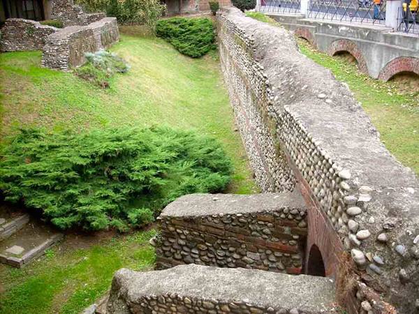 Ancient Roman pebble and brick walls, green lawn and shrubs