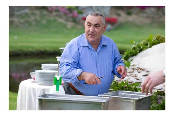 Chef in blue shirt shucking oysters at outdoor garden buffet