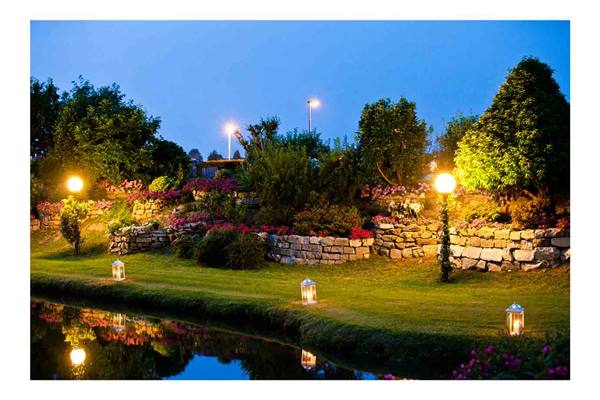 Flower garden with stone walls, lit lanterns and lights reflected in the pond