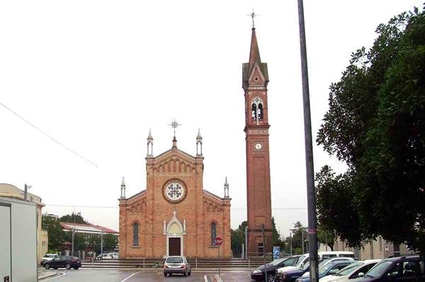 Brick church with rose window and bell tower, square with parked cars under grey sky