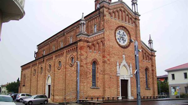 Brick church with rose window and spires under grey sky, cars parked in front