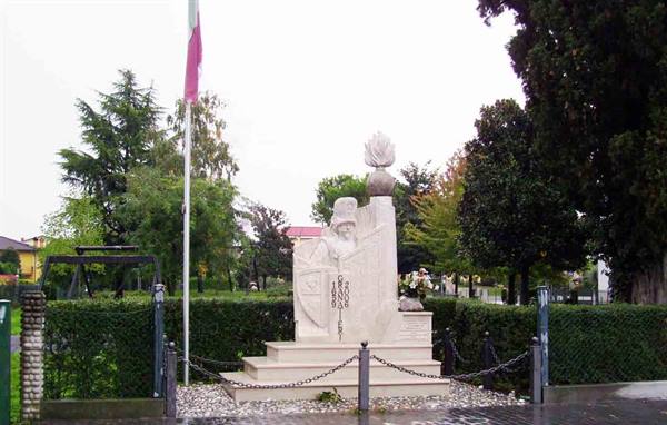 Marble monument with flame, carved doge, chains, tree-lined garden on a rainy day