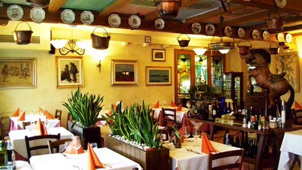 Trattoria dining room with set tables, decorative plates and hanging copper pots