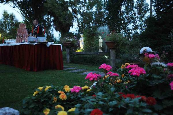 Multi-tier wedding cake on buffet table, pink flowers and statues in dusk garden