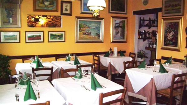 Trattoria dining room with set tables, white tablecloths and paintings on yellow walls