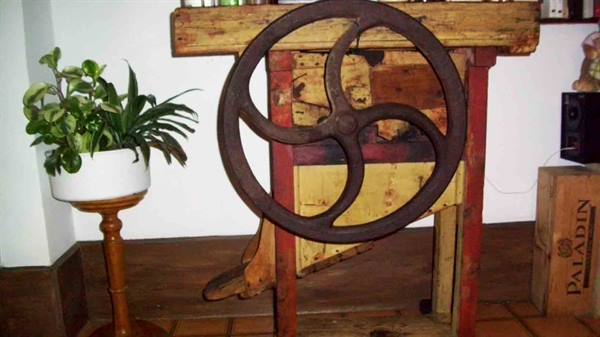 Cast iron wheel on wooden farm machine, potted plant nearby