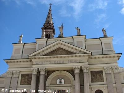 Neoclassical facade with columns, saint statues and tall bell tower under blue sky