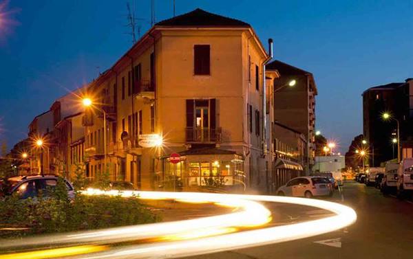 Evening urban intersection with yellow building, streetlights on and light trail