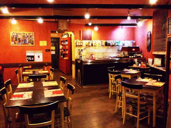 Trattoria dining room with wooden tables, bar counter, orange walls, warm lighting