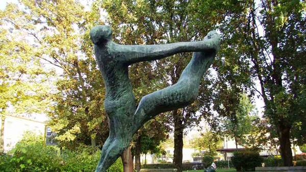 Green bronze sculpture of two dancing figures in a tree-filled park