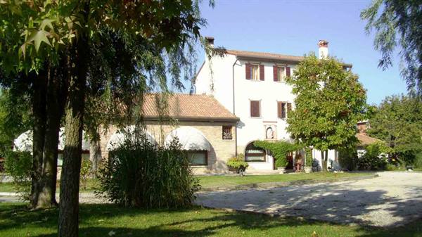White farmhouse with terracotta roofs among trees and green garden
