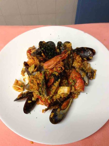 White plate with seafood rice: mussels, shrimp and calamari on pink tablecloth