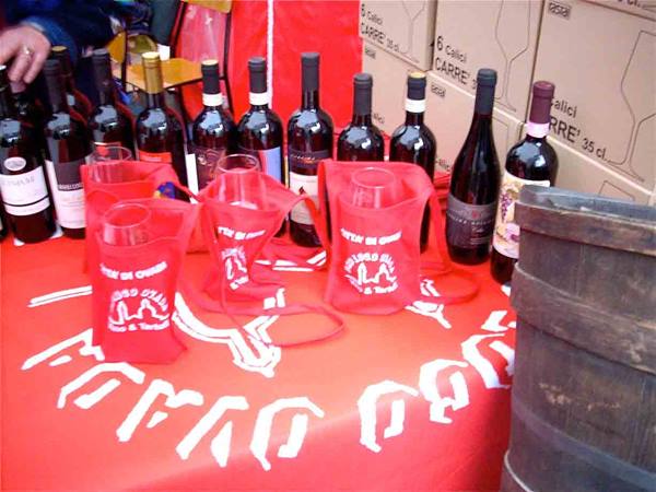 Wine bottles on red tablecloth with red tote bags and wooden barrel