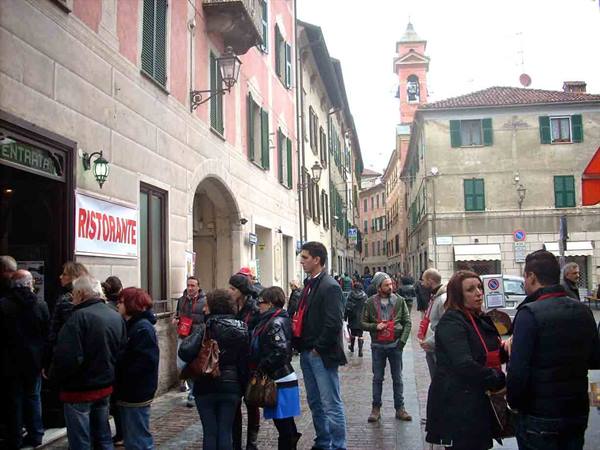Tourists queuing outside a restaurant on a narrow street with bell tower