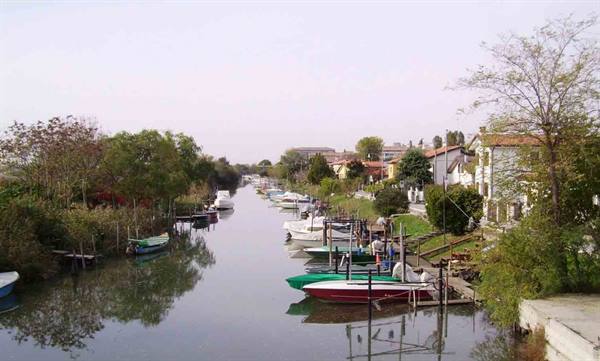 Boats moored along a canal with houses and trees on the banks