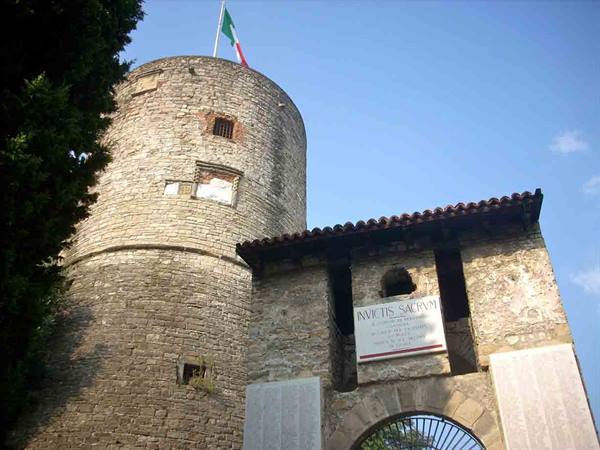 Cylindrical stone tower with Italian flag beside an inscribed gateway