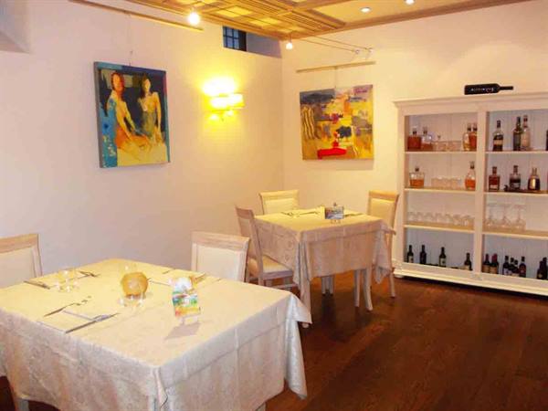 Restaurant dining room with set tables, colorful paintings and a liquor cabinet