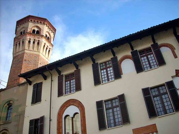 Medieval brick tower beside cream building with dark shutters under blue sky