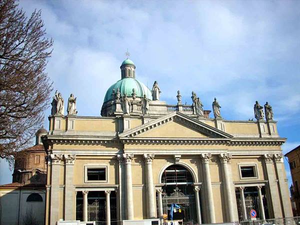 Stone cathedral facade with green dome and statues under a cloudy sky