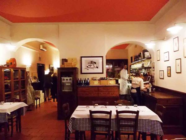Trattoria dining room with checkered tablecloths, red ceiling, waiter at counter