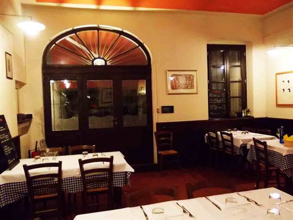 Trattoria dining room with set tables, checkered tablecloths and arched wooden door