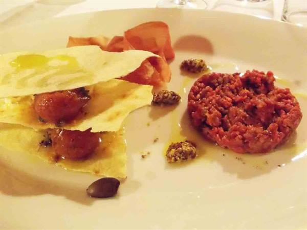 White plate with red beef tartare, crispy pastry layers and olives