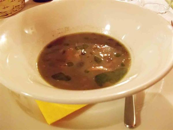 Dark herb soup served in a white bowl on the table
