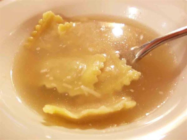 Ravioli in light broth, white bowl, steel spoon, warm light