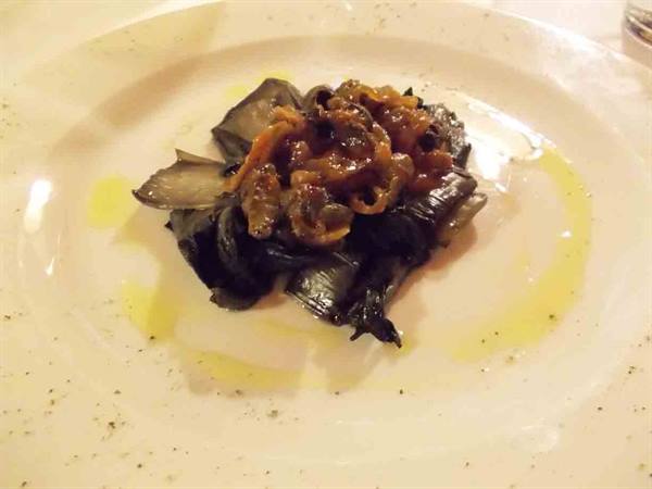 White plate with cooked dark vegetables, drizzled with oil, on a lit table