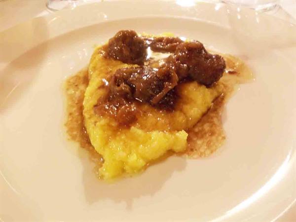 Yellow polenta topped with meat sauce, served on a white plate