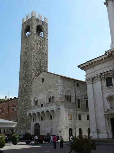 Crenellated stone tower beside the Broletto palace, people walking in Brescia square