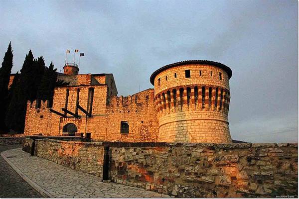 Brescia Castle: round stone tower lit by sunlight at dusk