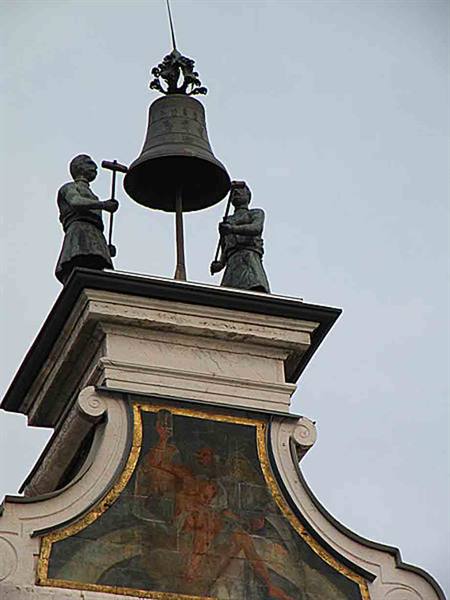 Two bronze statues hammer a bell atop a frescoed building gable