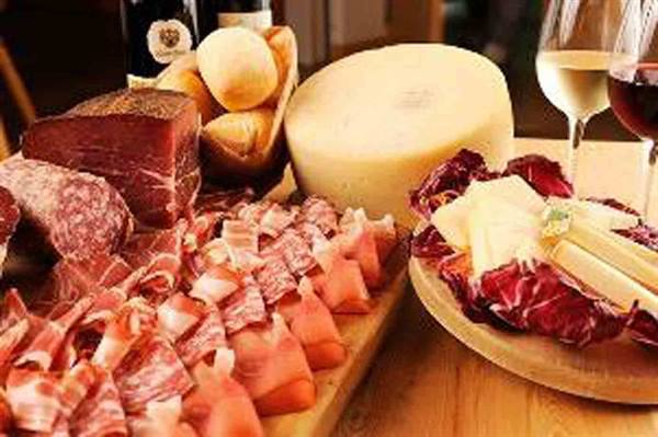 Wooden board with cured meats, cheeses, red and white wine glasses
