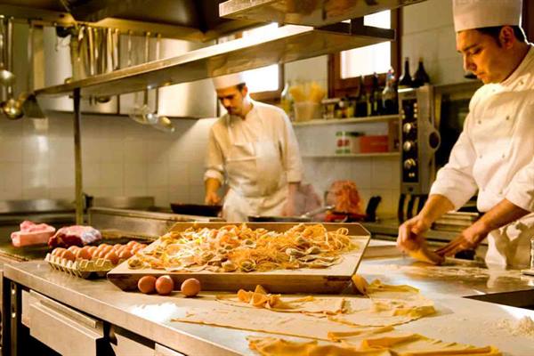 Chefs preparing fresh pasta on steel counter with eggs and dough in kitchen